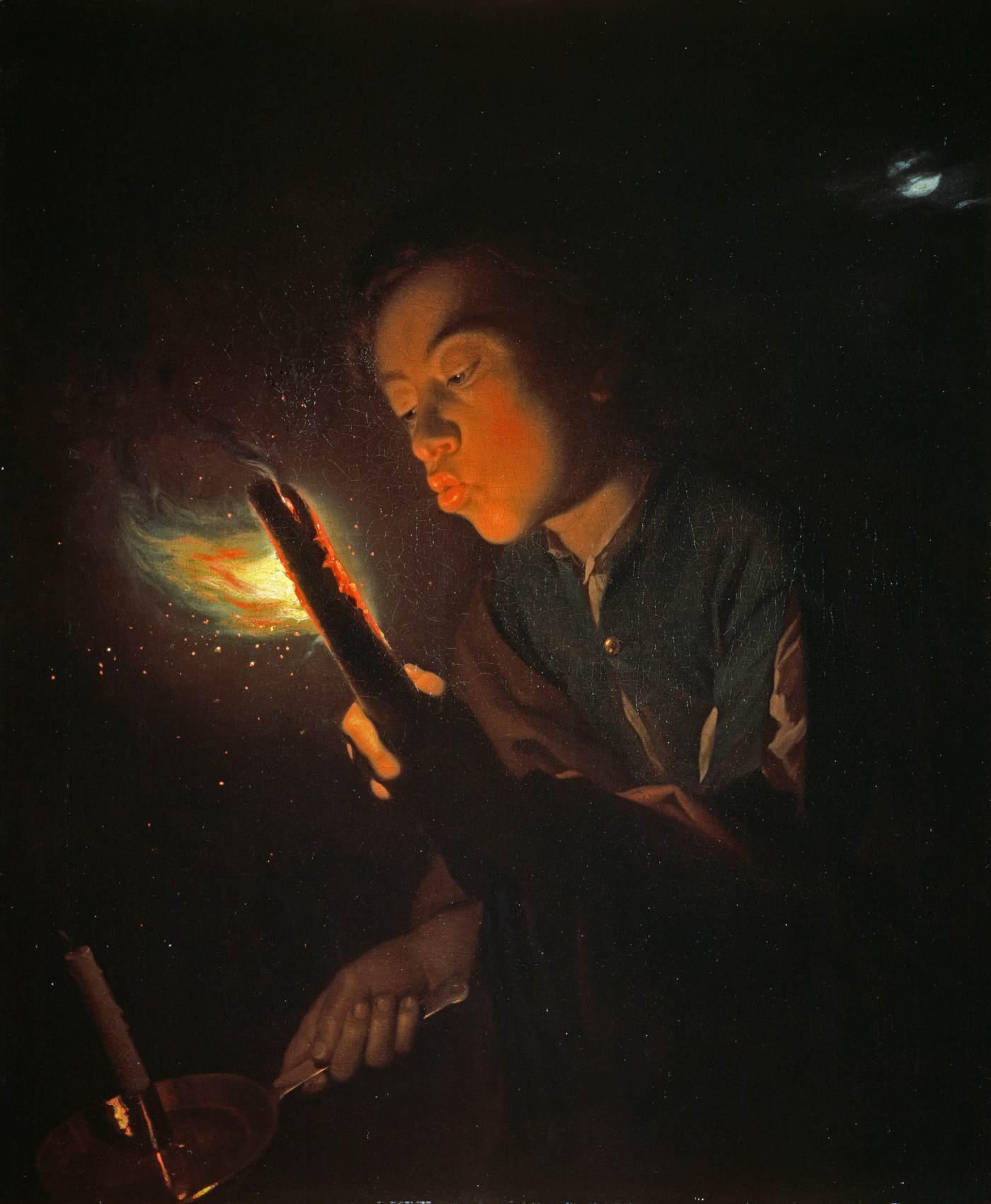 A Boy Blowing On A Brand Of Fire To Light A Candle